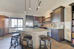 Kitchen featuring backsplash, stainless steel appliances, a center island, light stone counters, and vaulted ceiling