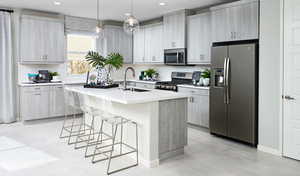 Kitchen with a kitchen bar, sink, a center island with sink, appliances with stainless steel finishes, and pendant lighting