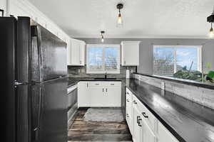 Kitchen with black fridge, decorative light fixtures, and white cabinets