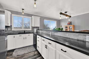 Kitchen with hanging light fixtures, white cabinetry, black dishwasher, and sink