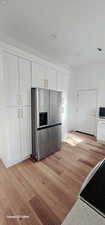 Kitchen with stainless steel fridge with ice dispenser, white cabinetry, range, light hardwood / wood-style floors, and light stone counters