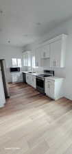 Kitchen with appliances with stainless steel finishes, sink, white cabinets, and light hardwood / wood-style floors