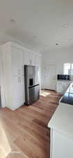 Kitchen with white cabinetry, light stone counters, light hardwood / wood-style flooring, and appliances with stainless steel finishes