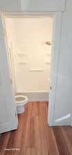 Bathroom featuring hardwood / wood-style floors, toilet, and washtub / shower combination