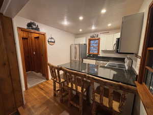 Kitchen with sink, a breakfast bar area, appliances with stainless steel finishes, white cabinetry, and dark hardwood / wood-style flooring