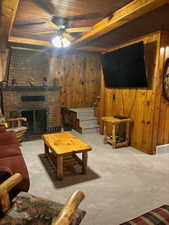 Furnished Living room with large Flat Screen TV, featuring ceiling fan, wooden walls, a fireplace, light carpet, and wooden ceiling