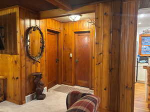 Doorway to outside with light colored carpet, beamed ceiling, and wood walls