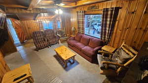 Furnished Living room featuring beamed ceiling, carpet flooring, wooden walls, and ceiling fan with notable chandelier