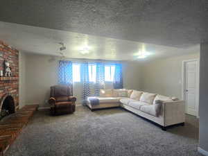 Living room with dark colored carpet, a brick fireplace, and a textured ceiling