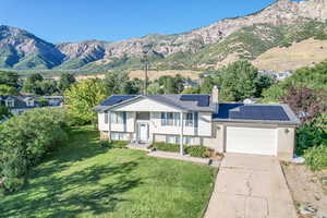 View of front of property with a garage, a mountain view, solar panels, and a front lawn