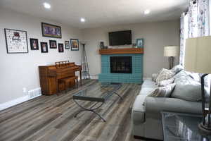 Living room with hardwood / wood-style floors, a textured ceiling, and a brick fireplace