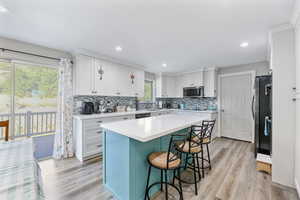 Kitchen with white cabinetry, a center island, light hardwood / wood-style flooring, a kitchen breakfast bar, and stainless steel appliances