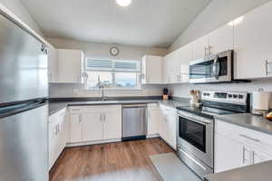 Kitchen with lofted ceiling, sink, white cabinetry, dark hardwood / wood-style floors, and stainless steel appliances