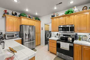 Kitchen featuring stainless steel appliances, washing machine and dryer, tile counters, and backsplash