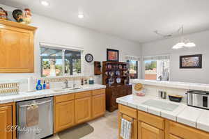 Kitchen featuring sink, tasteful backsplash, tile countertops, light tile patterned floors, and stainless steel dishwasher