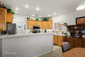 Kitchen featuring sink, tile countertops, light brown cabinets, light colored carpet, and stainless steel appliances