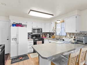 Kitchen with sink, white refrigerator with ice dispenser, gas stove, white cabinets, and kitchen peninsula