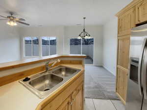 Kitchen featuring sink, stainless steel fridge with ice dispenser, light brown cabinets, pendant lighting, and light colored carpet