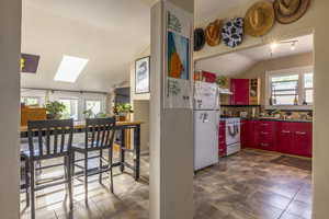 Kitchen featuring white appliances, a wealth of natural light, lofted ceiling with skylight, and decorative backsplash