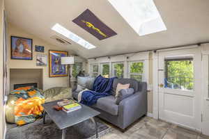 Living room with vaulted ceiling with skylight and light tile patterned flooring