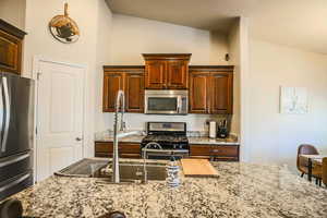 Kitchen with light stone counters, vaulted ceiling, and appliances with stainless steel finishes