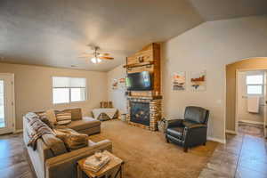 Living room featuring lofted ceiling, a textured ceiling, a fireplace, and ceiling fan