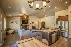 Kitchen featuring a stone fireplace, sink, a breakfast bar area, stainless steel appliances, and a center island with sink