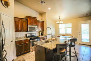 Kitchen featuring sink, a breakfast bar area, a kitchen island with sink, hanging light fixtures, and stainless steel appliances