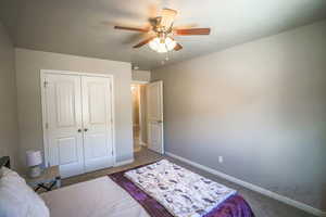 Carpeted bedroom with ceiling fan and a closet