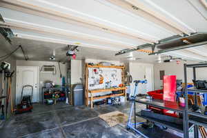 Garage featuring a garage door opener, gas water heater, electric panel, a wall unit AC, and a workshop area