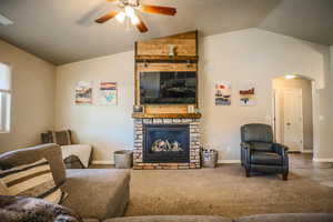 Carpeted living room with a fireplace, vaulted ceiling, and ceiling fan