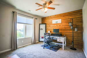 Home office featuring light carpet, ceiling fan, and rustic walls