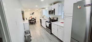 Kitchen with sink, appliances with stainless steel finishes, white cabinetry, tasteful backsplash, and light hardwood / wood-style floors