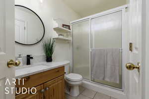 Bathroom with tile patterned floors, toilet, a shower with shower door, and vanity