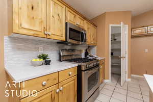 Kitchen featuring stainless steel appliances, tasteful backsplash, light tile patterned floors, and light stone counters