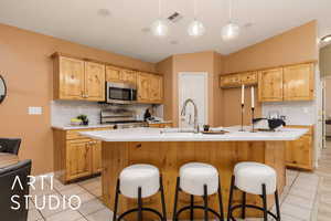 Kitchen with hanging light fixtures, an island with sink, range, and light tile patterned floors