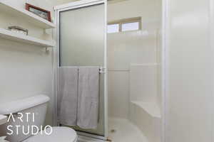 Bathroom featuring a shower with door and toilet