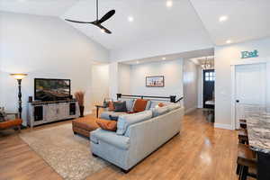 Living room featuring ceiling fan with notable chandelier, high vaulted ceiling, and light hardwood / wood-style flooring