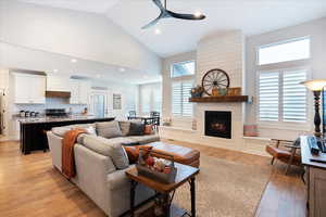 Living room with high vaulted ceiling, a large fireplace, sink, ceiling fan, and light wood-type flooring