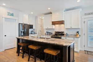 Kitchen featuring sink, stainless steel appliances, an island with sink, and white cabinets