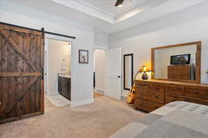 Bedroom with a raised ceiling, ensuite bathroom, a barn door, and light carpet