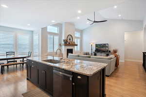 Kitchen featuring dishwashing machine, sink, a fireplace, light hardwood / wood-style floors, and a center island with sink