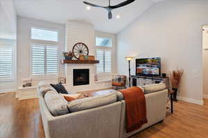 Living room featuring hardwood / wood-style flooring, ceiling fan, high vaulted ceiling, and a fireplace