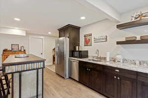 Kitchen featuring sink, dark brown cabinetry, stainless steel appliances, light stone countertops, and light hardwood / wood-style flooring