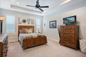 Bedroom with a raised ceiling, light colored carpet, and ceiling fan