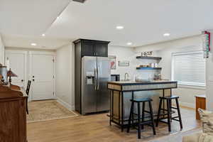 Kitchen with sink, stainless steel fridge, a breakfast bar area, light hardwood / wood-style floors, and an island with sink