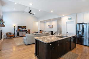 Kitchen with a fireplace, dishwasher, sink, stainless steel fridge, and a center island with sink