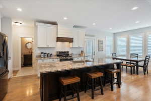 Kitchen with black refrigerator, sink, white cabinets, a kitchen island with sink, and stainless steel range with gas stovetop