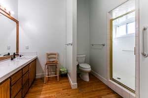 Bathroom featuring wood-type flooring, toilet, a shower with shower door, and vanity