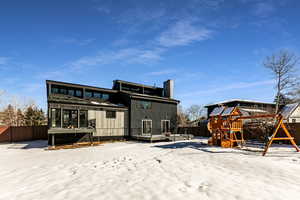 Snow covered rear of property with a playground and a deck